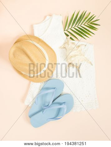 Summer fashion summer outfit on cream background. White lace dress blue flip flops seashell and straw hat. Flat lay top view