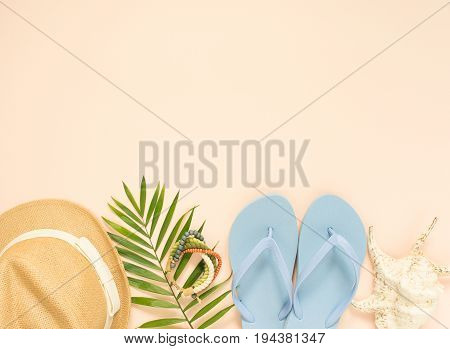 Summer fashion summer outfit on cream background. Blue flip flops seashell wood bracelet and straw hat. Flat lay top view