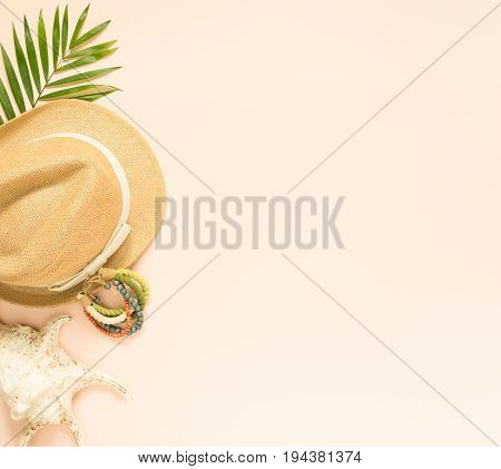 Summer fashion summer outfit on cream background. Seashell wood bracelet and straw hat. Flat lay top view.