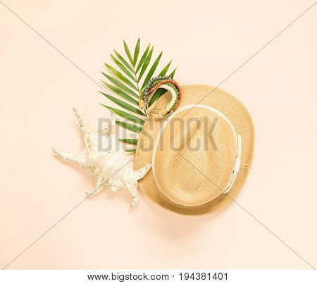 Summer fashion summer outfit on cream background. Seashell wood bracelet and straw hat. Flat lay top view.