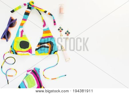 Summer outfit beach outfit summer stuff. Geometric abstract pattern swimsuit bright sunglasses and earrings. Flat lay top view.