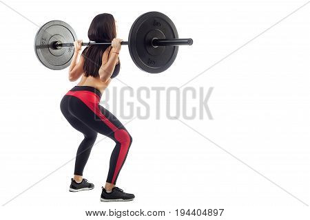 Young athletic brunette woman in black leggings with a red strip doing squat with a barbell hands behind her shoulders rear view position of a half-breed on a white isolated background