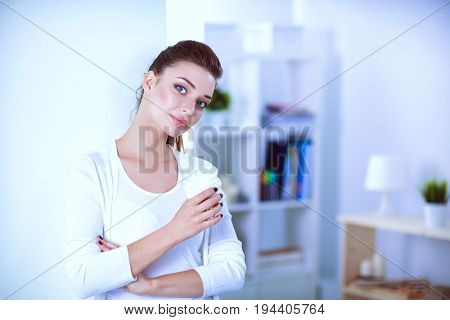 Young woman drinking cup coffee near wall