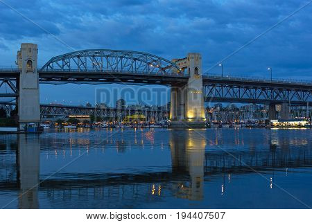 VANCOUVER, CANADA - JUNE 26: Burrard Bridge at dawn Granville Public Market with in a view on June 26 2017 in Vancouver Canada. Steel truss bridge over False Creek with imposing concrete towers before sunrise.