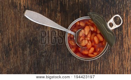 Canned beans in a tin with spoon on wooden background with copy space