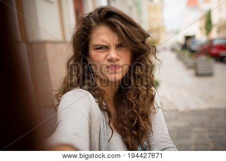 Tourist woman in the street on selfie shot showing gloomy face. Curly girl showing emotions of dissatisfaction.