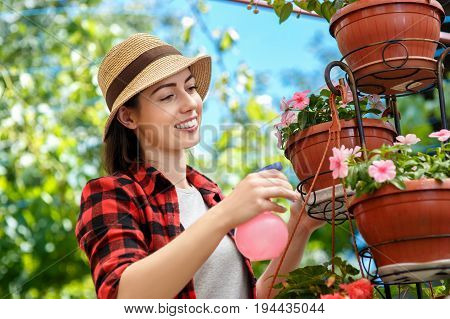 portrait of happy young woman gardener spraying water on plants. Girl with sprayer bottle spraying pesticide on her flowers. People, gardening, care of flowers, hobby concept