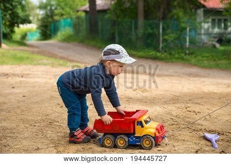Little boy 2-3 years old playing outdoors with a plastic truck