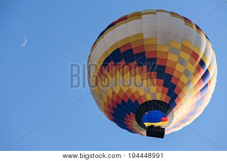 Colorful hot-air balloon in flight and moon seen from below against a blue sky