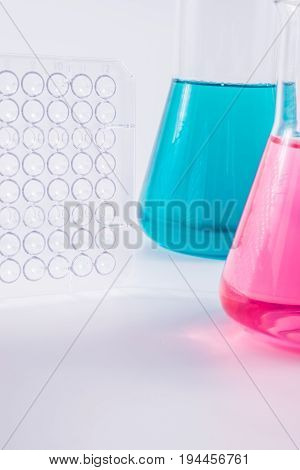research, science and clinic background. 96 well micro plate and  laboratory beakers with colorful liquids and reagents.