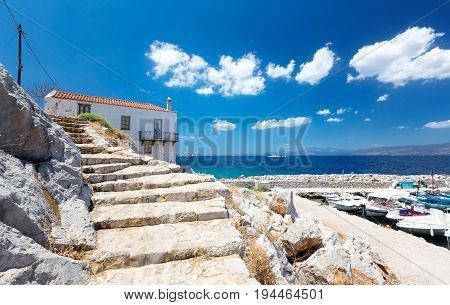 Travel Greece. View from Hydra Island. Traditional Greek house. Castello Hydra and Kamini beach. Blue sky with soft white clouds