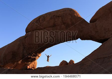 Young Girl Jumping  At Stone Arch Of Spitzkoppe. Concept Of Extreme And Ecological Tourism. Natural