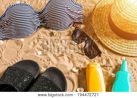 Summer bikini and accessories stylish beach set, Beach bikini summer outfit and sea sand as background, Top View, Concept. Copy space. Sun flare