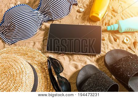Summer bikini and accessories stylish beach set, Beach bikini summer outfit and sea sand as background, Top View, Concept. Copy space. Sun flare
