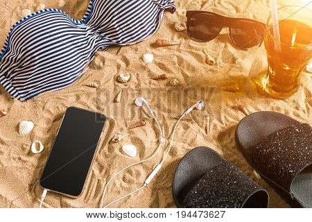 Summer bikini and accessories stylish beach set, Beach bikini summer outfit and sea sand as background, Top View, Concept. Copy space. Sun flare
