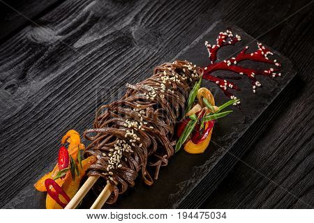 soba noodles of buckwheat Noodles of buckwheat yellow and red pepper, herbs. Pan-Asian cuisine. On stone tray on dark wooden table. Place for text.
