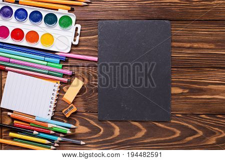 Back to school. Different stationery - pencils pen note erazer paint and empty slate board on wooden background. Top view. Place for text.