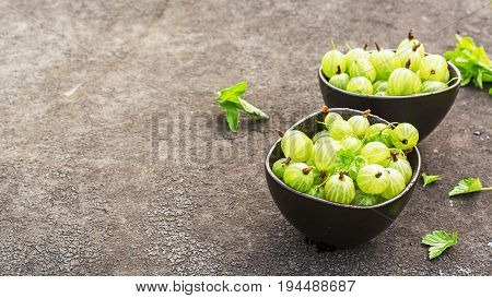 Fresh green gooseberries in a ceramic bowl on a dark background. Top view.