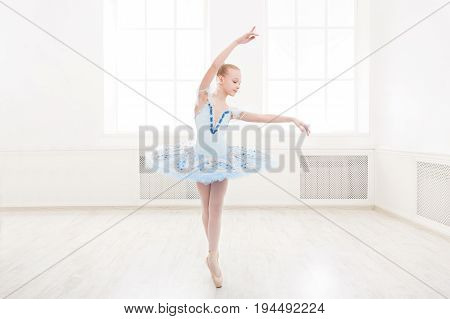 Young teenager ballerina practicing classical dance pas in studio before performance. Ballet student exercising in ballet costume, standing on her toes.
