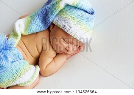 lovely newborn baby in knitted hat and panties sleeps curled up, top view