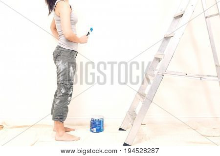 Low section of young woman holding paintbrush in unrenovated house