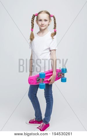Kids Concepts and Ideas. Full Length Portrait of Little Caucasian Blond Girl with Nice Pigtails Posing With Pink Pennyboard Against White Background. Vertical Shot