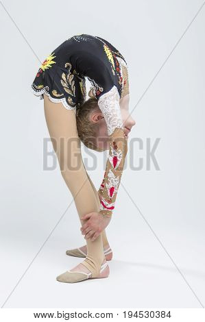 Sport concepts and Ideas. Young Caucasian Female Rhythmic Gymnast Athlete In Professional Competitive Suit Doing Backbend Stretching Exercise While Posing in Studio Against White. Vertical Composition