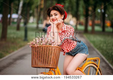 Pinup woman on bicycle with backet of flowers
