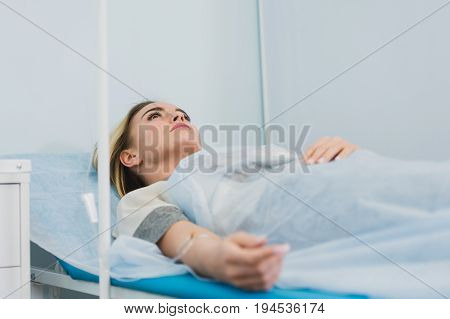 Pensive woman transfused lying in hospital ward.