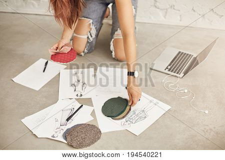 Close up of fashion designer in a middle of her work using laptop and drawing skethes and illustrations of her new collection