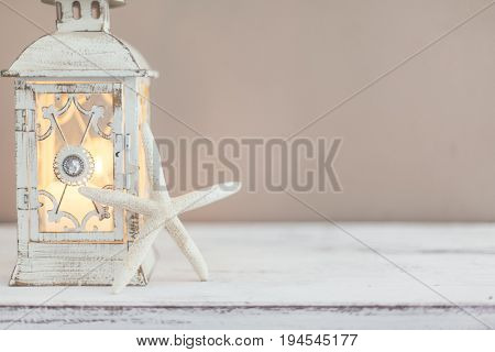 Beach wedding interior decor. Natural seashell and lantern on vintage shelf over pastel wall.