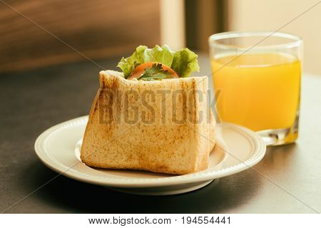 Pocket sandwich for breakfast or lunch. Homemade sandwich with boiled eggs and mayonnaise decorated by lettuce and tomato. Baked sandwich on white plate serve with orange juice on granite table. Delicious grilled sandwich ready to served.
