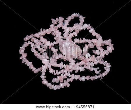 Tumbled rose quartz stone surrounded by rose quartz strings on black background