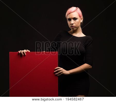 Young sexy woman portrait of a confident businesswoman showing presentation, pointing red placard, bkack background. Ideal for banners, registration forms, presentation, landings, presenting concept.