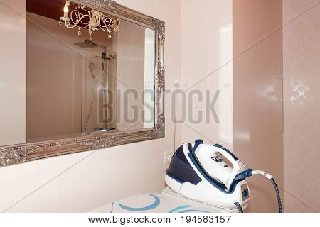 Steam iron, steamer with ironing board in modern bathroom interior