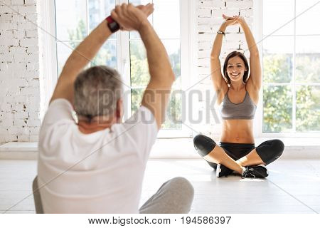 Sport for everybody. Active pensioner sitting in yoga pose and holding arms upwards while posing with back on camera