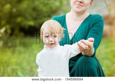 Cute little girl with big eyes standing in front of mom and holding her hand