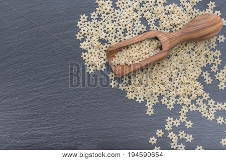Star shaped noodles and olive wood scoop on black background of slate or stone. Top view