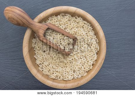 Star shaped noodles in a wooden bowl and olive wood scoop on black background of slate or stone. Top view