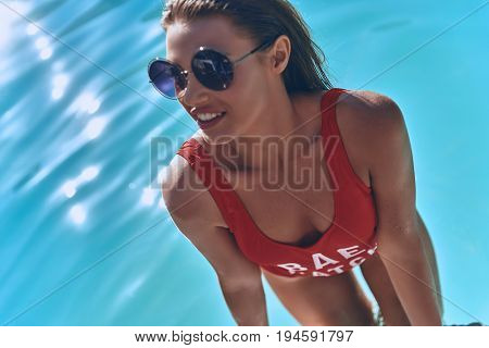 Gorgeous beauty. Top view of attractive young woman in swimwear smiling while getting out the swimming pool