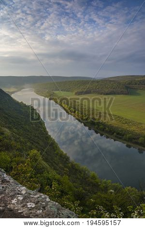 Top view of Dnestr (Dniester) river in morning. Blue sky with clouds reflects in water. Thin mist covers part of river.