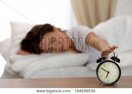 Sleepy young woman stretching hand to ringing alarm willing turn it off. Early wake up, not getting enough sleep, getting work concept