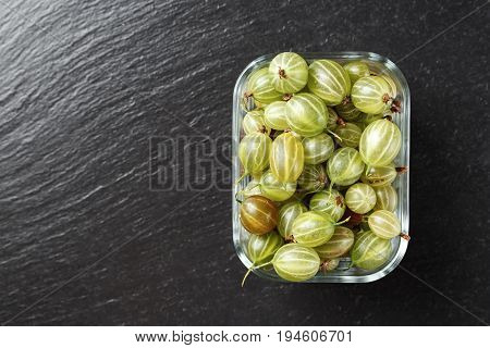 Ripe raw gooseberry in glass rectangular dishes on a black slate background space for text