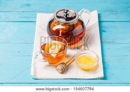 Glass cup of tea with lemon, glass teapot and honey on blue wooden table.