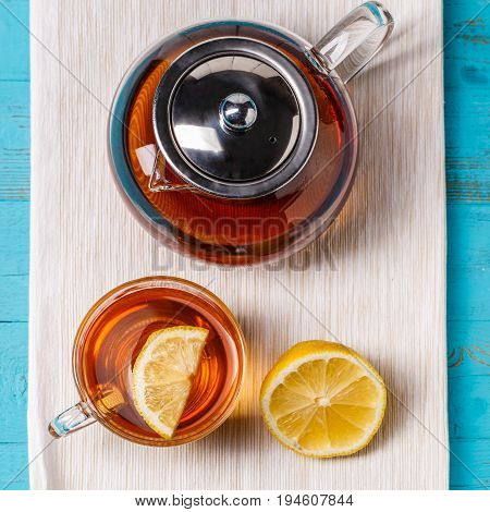 Glass cup of tea with lemon and glass teapot on blue wooden table.