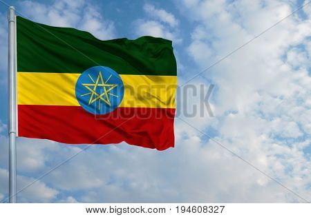National flag of Ethiopia on a flagpole in front of blue sky.