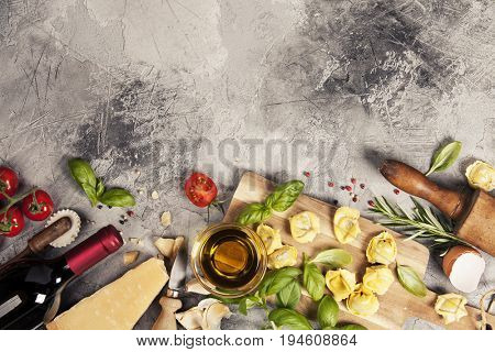 Italian food background with ravioli, vine tomatoes, basil, spaghetti, spinach, onion, parmesan, olive oil, garlic, peppercorns, rosemary and wine. Slate background 