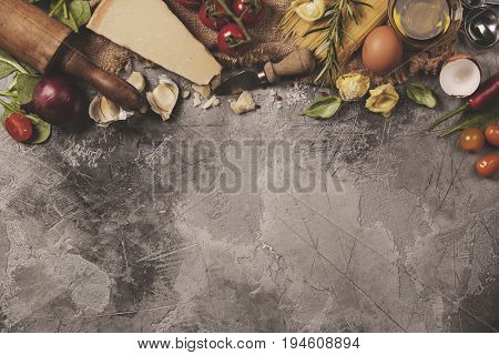 Italian food background with vine tomatoes, basil, spaghetti, spinach, onion, parmesan, olive oil, garlic, peppercorns, rosemary and eggs. Slate background 