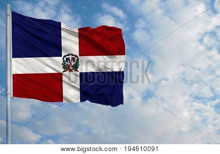 National flag of Dominican Republic on a flagpole in front of blue sky.