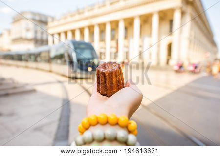 Holding a traditional Bordeaux sweet cake called Canele outdoors on the street near the Grand theatre building in Bordeaux